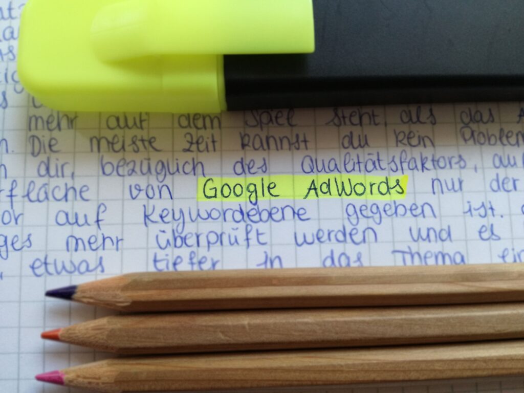 Close-up of colorful pencils on handwritten notes with Google AdWords highlighted.